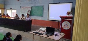 a white kitten with brown and black spots sitting with its paws slightly outstretched.